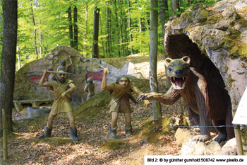 Steinzeitmenschen jagen mit Speeren ein Tier vor seiner Höhle